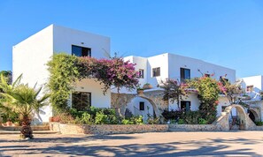 Un edificio bianco con numerose finestre e archi, circondato da vegetazione lussureggiante e piante fiorite.