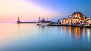 A calm waterfront with a historic building and a lighthouse in the background. - Villa Galini Sifis (Apokoronas)