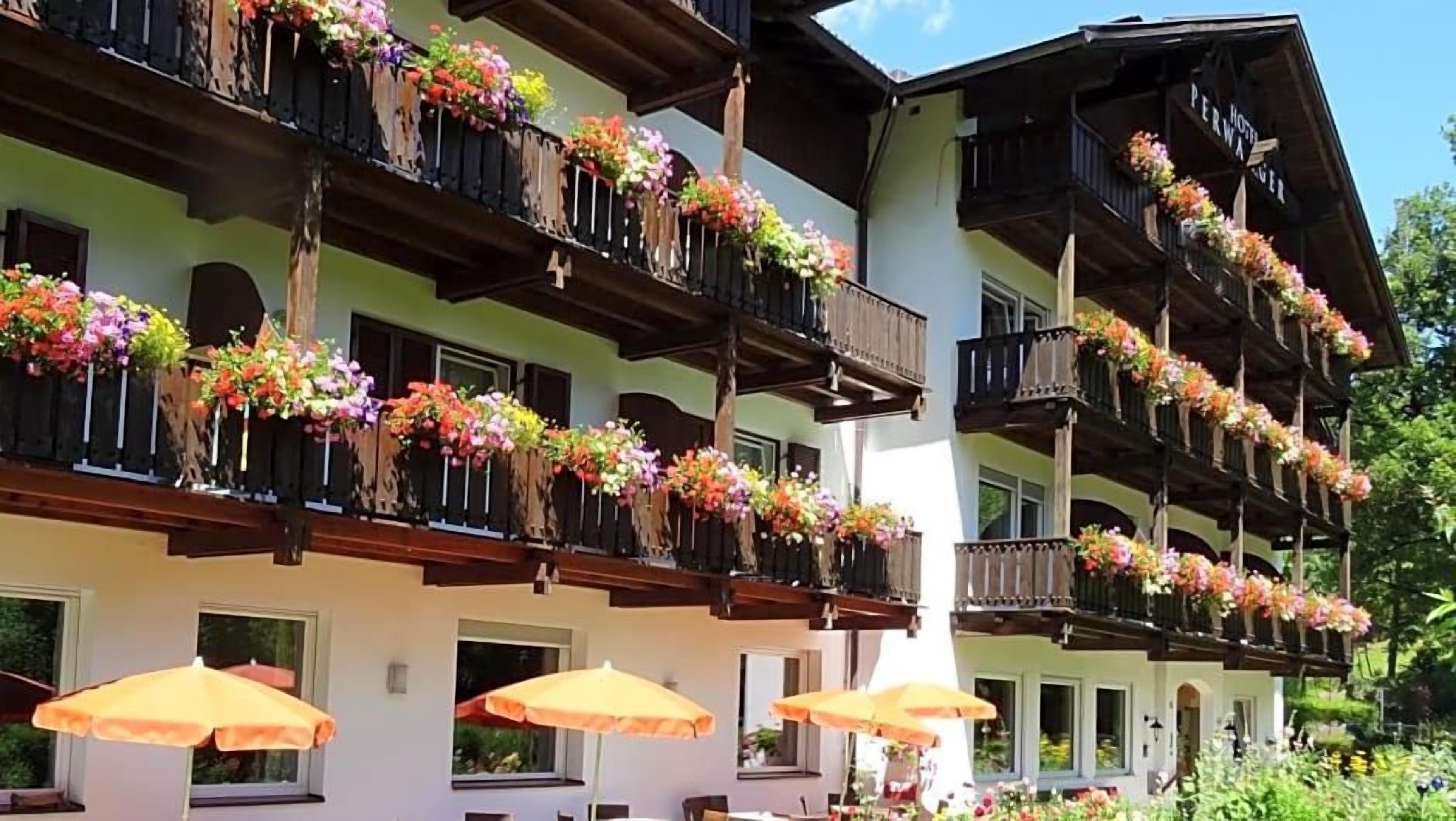 A hotel with multiple balconies adorned with colorful flowers, outdoor seating with umbrellas, and a traditional architectural style.