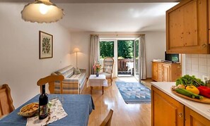 A cozy living room with a sofa, a dining table with a bottle and snacks, a kitchen with wooden cabinets and a TV, and a sliding glass door leading to a balcony. - Perwanger (Fie allo Sciliar)