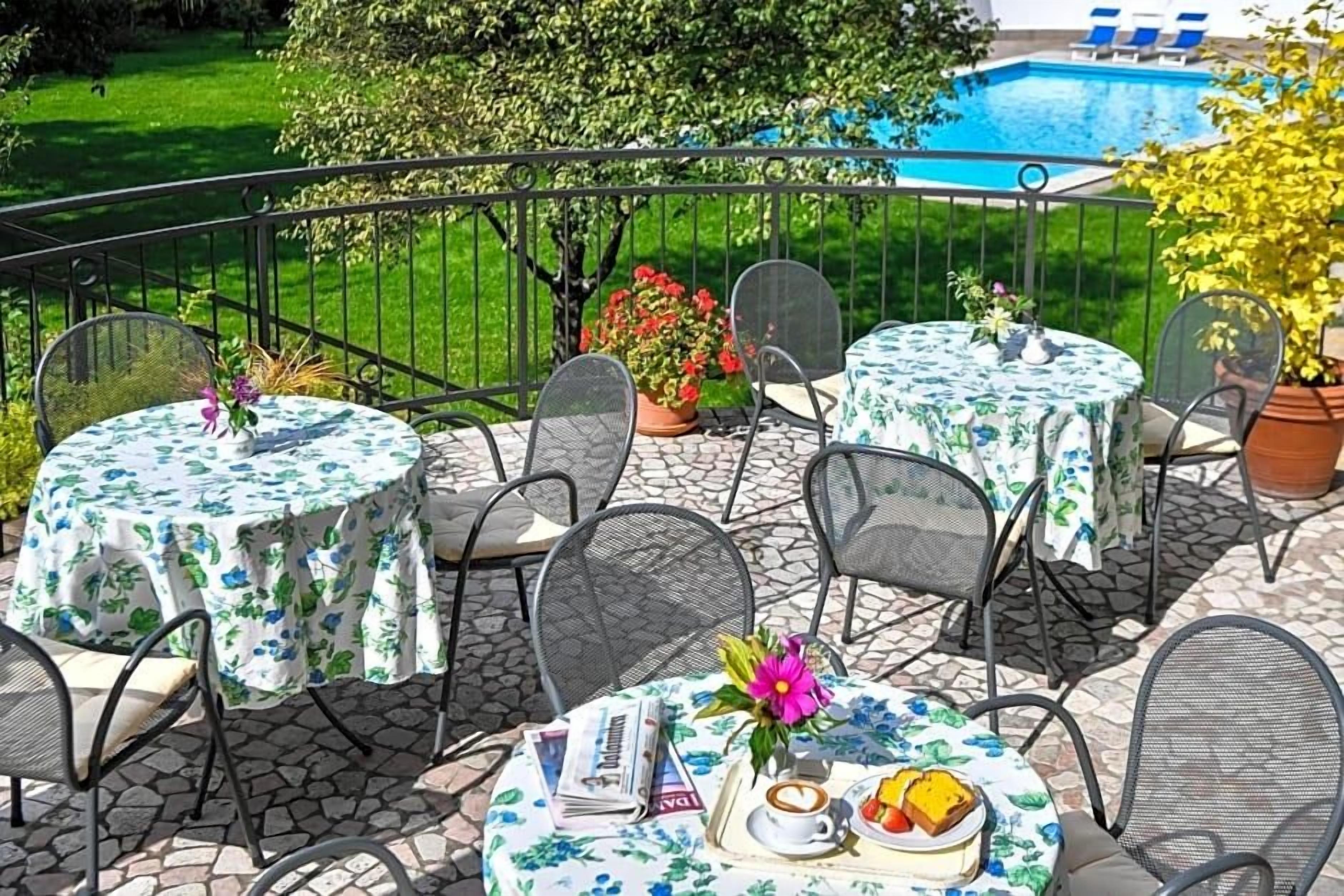 Une terrasse avec des tables et des chaises rondes, une piscine en arrière-plan et des plantes en pot.