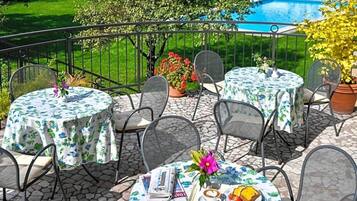 Eine Terrasse mit runden Tischen und Stühlen, im Hintergrund ein Pool und Kübelpflanzen.