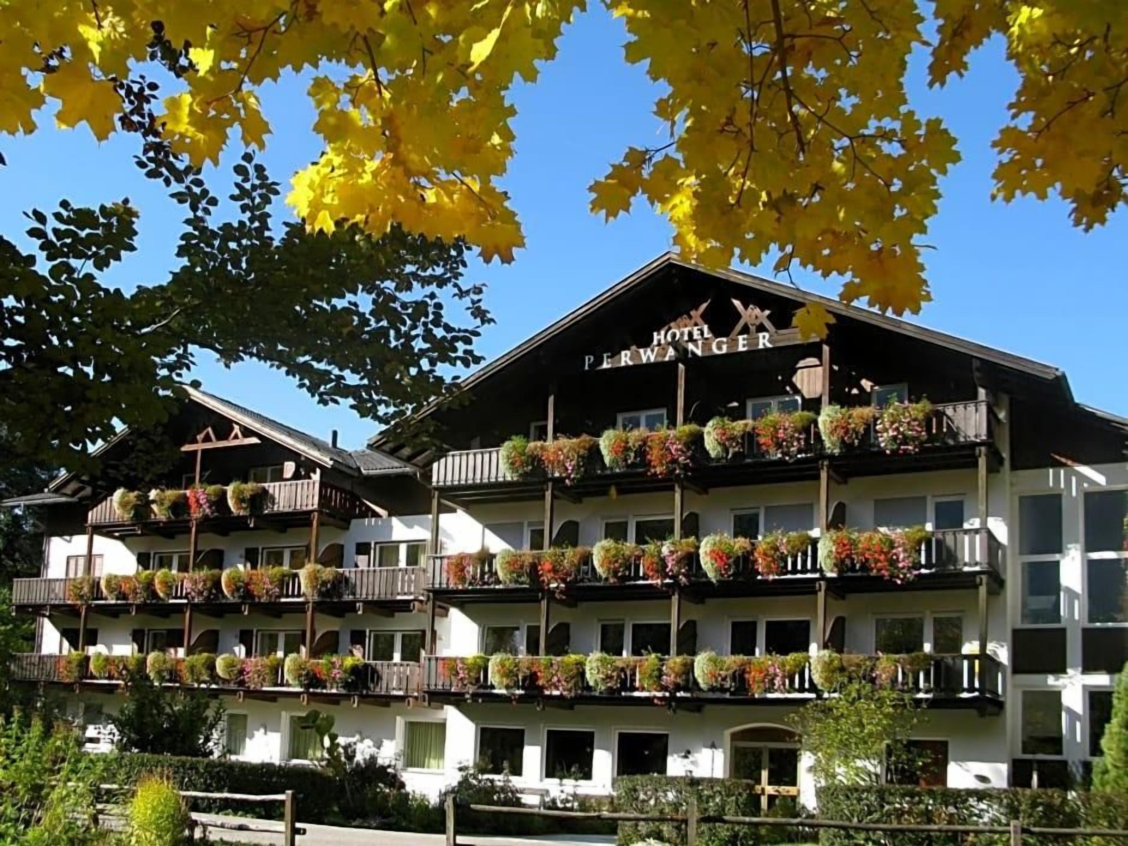 A hotel with multiple balconies adorned with flowers, a clear blue sky, and autumn leaves.