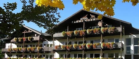 A hotel with multiple balconies adorned with flowers, a clear blue sky, and autumn leaves.