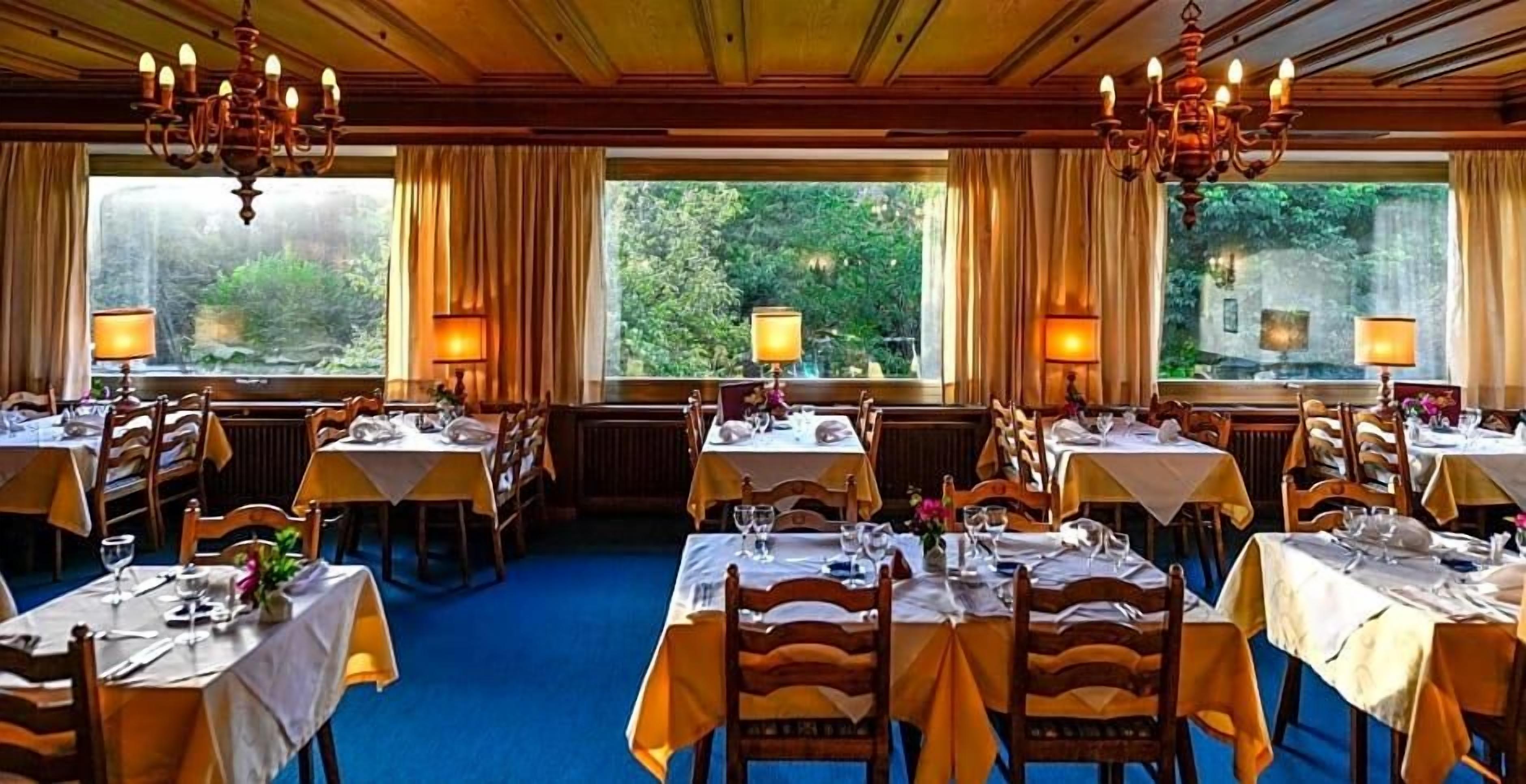 Ein Restaurant mit mehreren Tischen, gedeckt mit Besteck und Gläsern, und Kronleuchtern an der Decke.