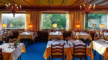 Ein Restaurant mit mehreren Tischen, gedeckt mit Besteck und Gläsern, und Kronleuchtern an der Decke.