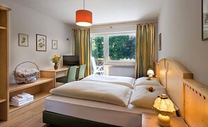 A hotel room with a bed, bedside lamps, a desk with a computer, a chair, a window with curtains, and a view of greenery outside. - Perwanger (Fie allo Sciliar)