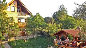 Une cabane en bois dotée d’un balcon, entourée d’un jardin avec un chemin de pierres et des parterres de fleurs.