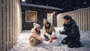 Eine Familie baut einen Schneemann in einer verschneiten Winterlandschaft, im Hintergrund ist ein Holzbauwerk zu sehen.
