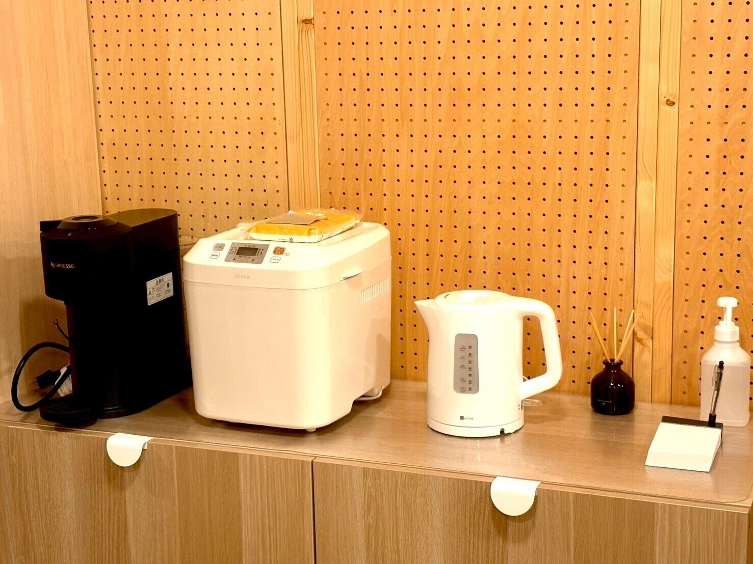 A kitchenette area with a coffee maker, a rice cooker, a kettle, and a bottle of hand sanitizer.