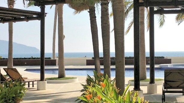 A poolside area with palm trees, a pool, and a view of the ocean. - Wohnung mit Whirlpool by Interhome (Acapulco de Juarez)