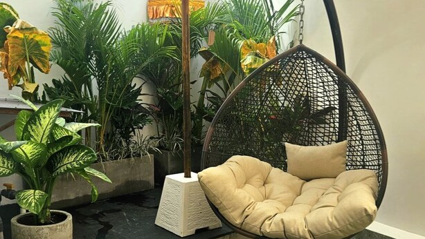A hanging chair with cushions, a small water feature, and a large umbrella in a courtyard with potted plants and a decorative wall. - Villa Shantila by Interhome (Denpasar)