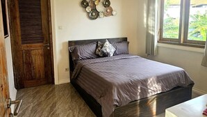A bedroom with a bed, a ceiling fan, a wall-mounted air conditioner, a wooden door, and a window with curtains. - Villa Shantila by Interhome (Denpasar)