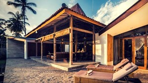 A beachside resort with a covered outdoor area, lounge chairs, and a dining space.