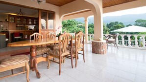 A spacious patio with a wooden table and chairs, a stone accent, and a view of lush greenery. - Erdgeschosswohnung mit Grill in Mare Anglaise by Interhome (Beau Vallon)