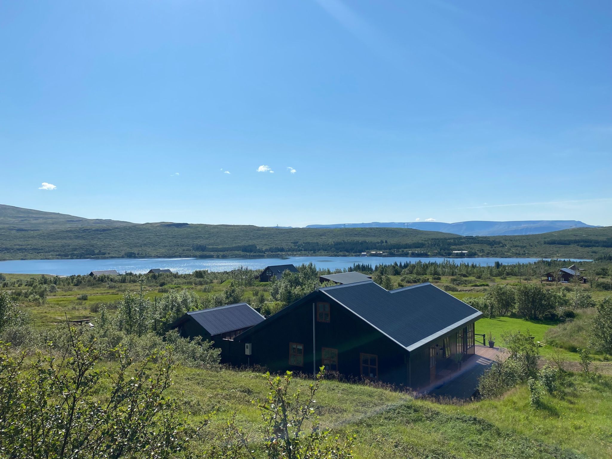 A modern house with a large deck, surrounded by lush greenery and a lake.