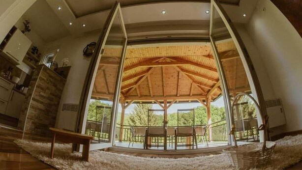 Una habitación amplia con techo alto, vigas de madera y un gran ventanal con vistas a un balcón con sillas.