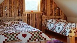 Ein Zimmer mit Holzwänden und schrägverdeckter Decke, mit zwei Betten mit gemusterten Bettdecken.