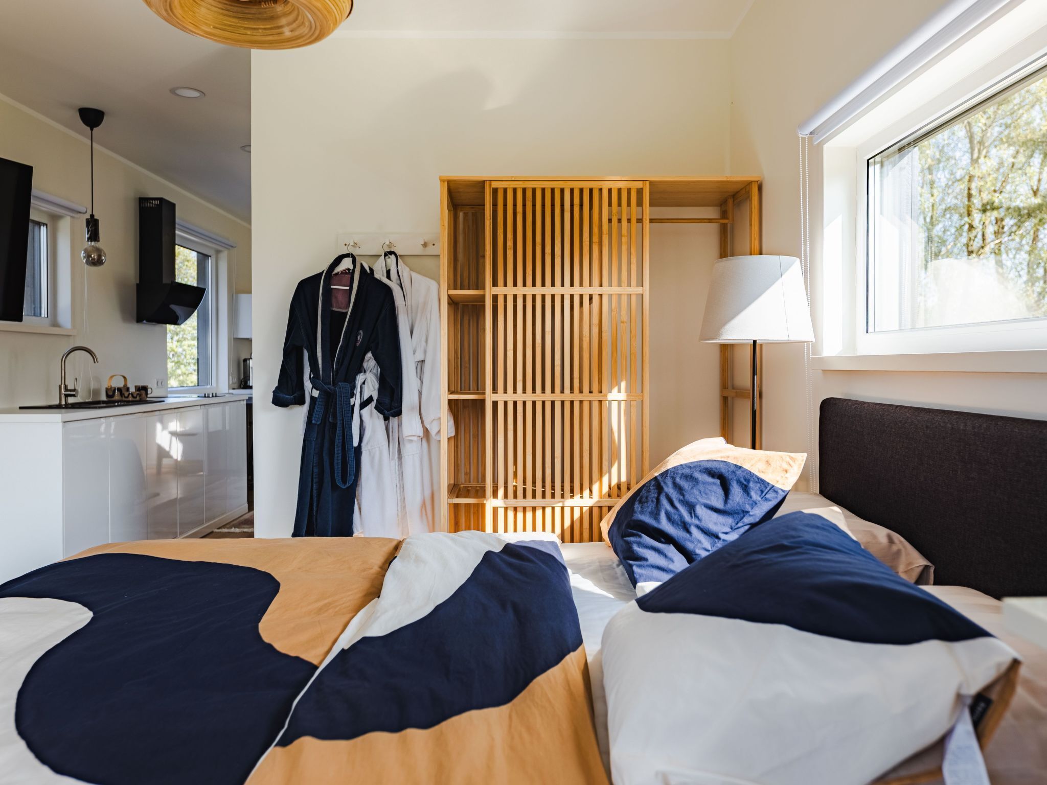 A modern hotel room with a bed, a wooden wardrobe, a sink, and a window with a view of trees.