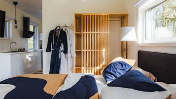 A modern hotel room with a bed, a wooden wardrobe, a sink, and a window with a view of trees.