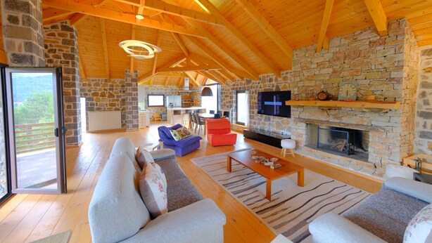 Un salón amplio con chimenea de piedra, vigas de madera en el techo y un sofá grande.