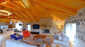 Amplia sala de estar con chimenea de piedra, vigas de techo de madera y pared de piedra.