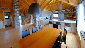 Una cocina amplia con pared de piedra, vigas de madera en el techo y una gran mesa de comedor con sillas.