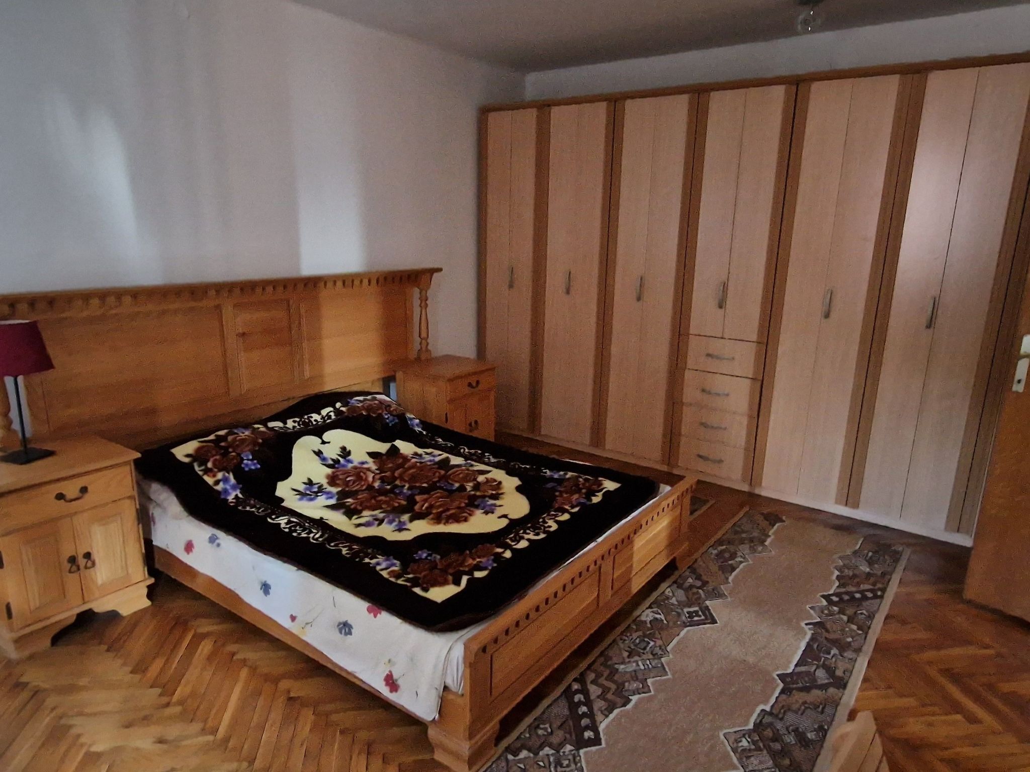 Ein Schlafzimmer mit einem hölzernen Bett, einem Nachttisch, einem Kleiderschrank und einem gemusterten Teppich.