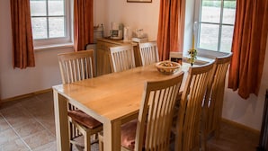 A dining area with a wooden table and chairs, a coffee maker, and a window with curtains. - Fuchsbau in Waldnähe by Interhome (Kuldiga)