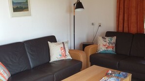 A living room with a black sofa, a wooden coffee table with magazines, a floor lamp, and a painting on the wall. - Fuchsbau in Waldnähe by Interhome (Kuldiga)