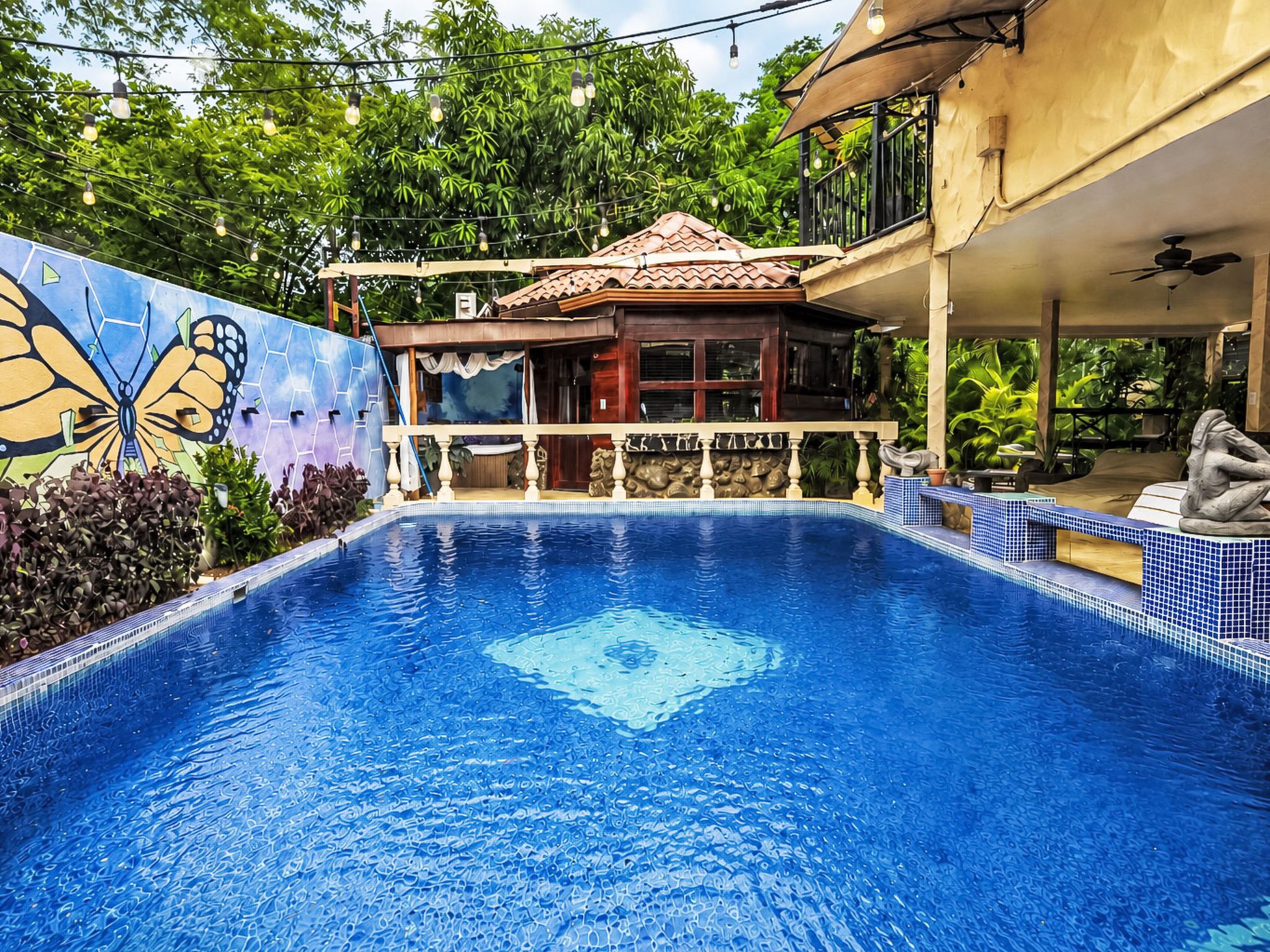 A swimming pool with a tiled edge, a butterfly mural, and a building with a balcony.
