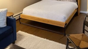 Une chambre à coucher moderne avec un cadre de lit en bois, un grand miroir, une chaise bleue et une petite table.