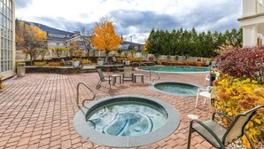 Un espace spa comprenant deux bains à remous et une piscine, entouré d’un sol en briques et de coins salons extérieurs.