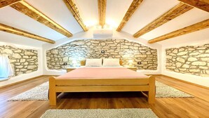 A bedroom with a stone wall, wooden beams, a bed, and an air conditioning unit. - Villa Balarini (Istria - Labin) (Šumber)