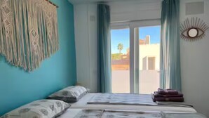Una camera da letto con un letto, cuscini, un arazzo macramè e vista sull'esterno.