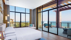 Un dormitorio amplio con una cama grande, un balcón con vistas al mar y un paisaje urbano al fondo.