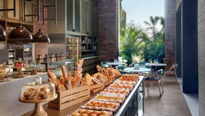 Un bufé de desayuno con diversos pasteles y pan, una estación de café y una zona de estar con mesas y sillas.