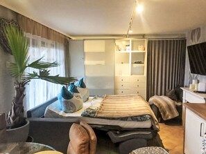 Et kompakt hotelværelse med seng, skrivebord, garderobeskab og en stor stueplante.