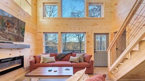 En mysig trästuga med en öppen spis, en röd soffa och en trappa.