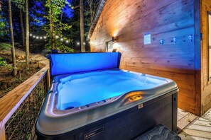 A hot tub in front of a wooden cabin with a sign indicating hot tub availability. - Skyward Chalet - Hot Tub - Fire Pit - Deck - RRG (Stanton)
