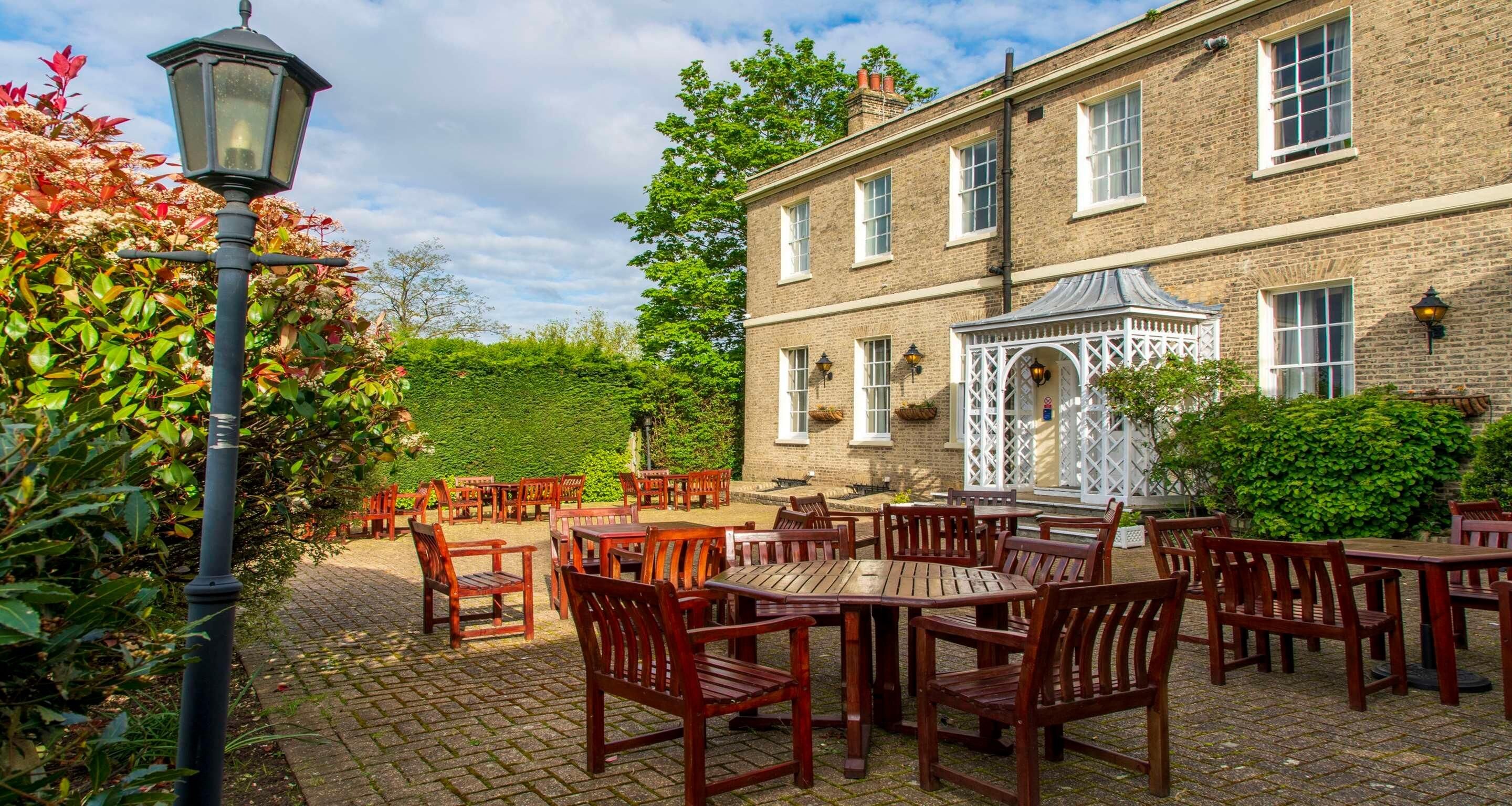 A brick building with a garden patio featuring wooden tables and chairs.
