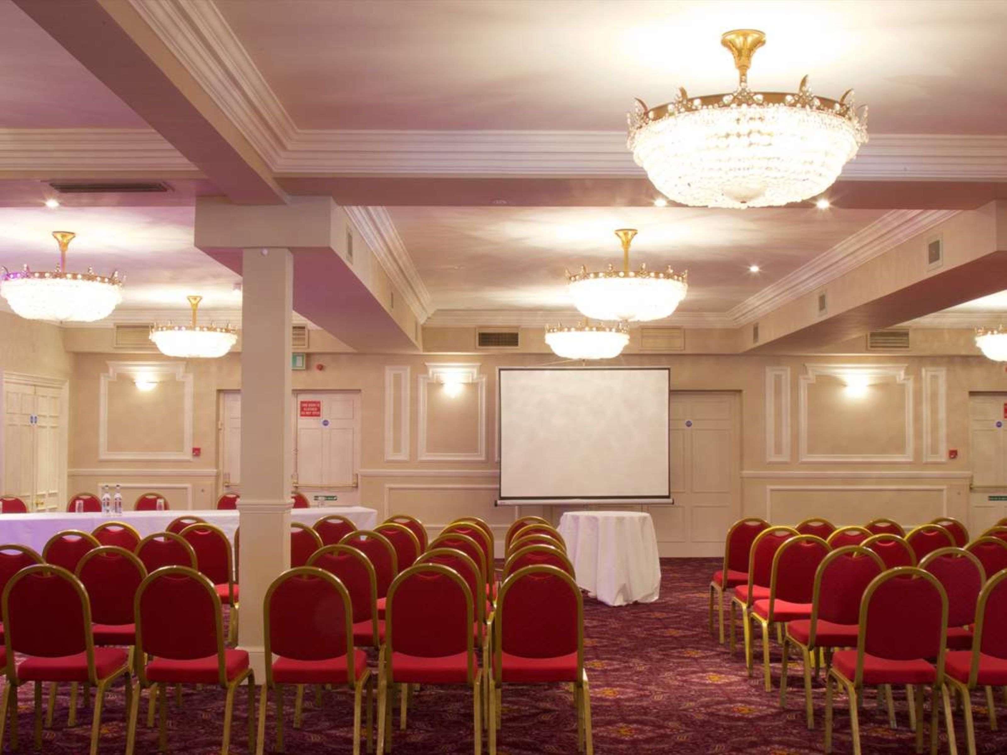 A conference room with rows of red chairs, a whiteboard, and chandeliers.