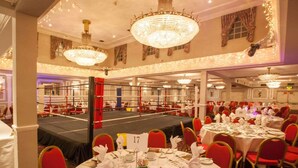 Ein Festsaal mit runden Esstischen, einer Boxarena in der Mitte und Kronleuchtern an der Decke.