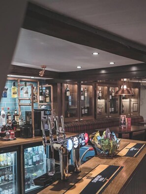 A bar area with multiple taps, a refrigerator stocked with beverages, and a seating area with a couch and table. - Olde Kings Arms (Hemel Hempstead)