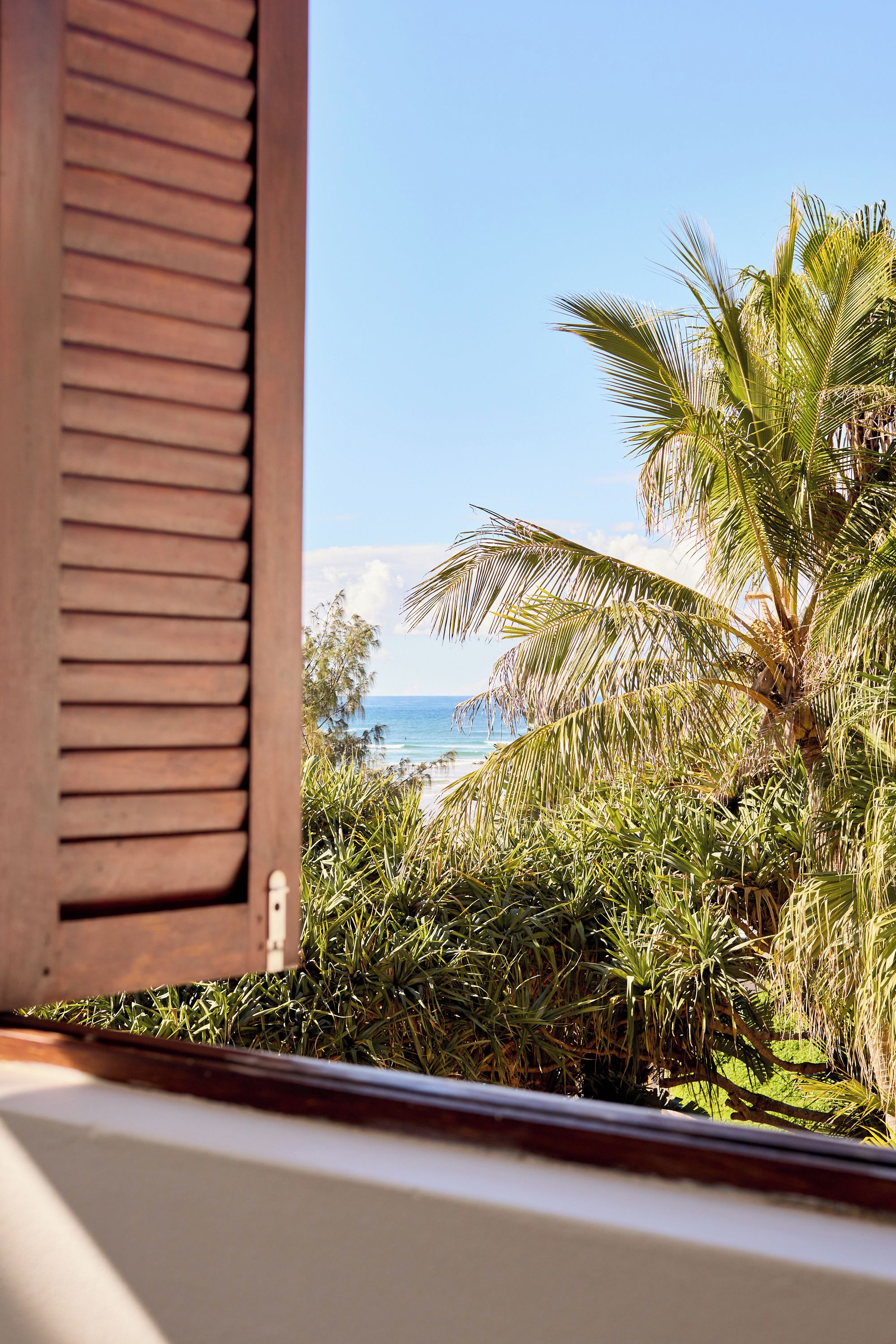 Une fen être avec des volets en bois, une vue sur une plage et des palmiers.