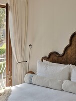 Un dormitorio con cabecera de madera, ropa de cama blanca y vistas al exterior.