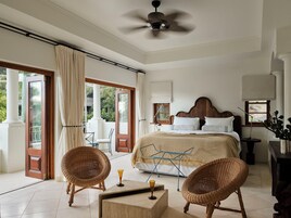 Un dormitorio con una cama, dos sillones de mimbre, una mesita y un ventilador de techo.