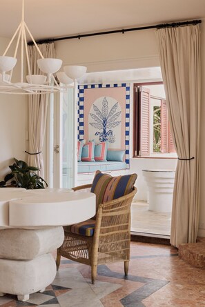 A room with a wicker chair, a white sofa with patterned cushions, a white table, and a view of the outdoors through an open door. - Raes on Wategos (Byron Bay)