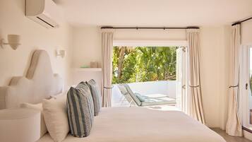 A bedroom with a bed, pillows, a nightstand, a lamp, and a view of a balcony with outdoor furniture.