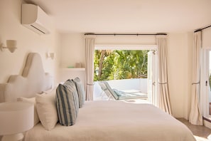 A bedroom with a bed, pillows, a nightstand, a lamp, and a view of a balcony with outdoor furniture. - Raes on Wategos (Byron Bay)